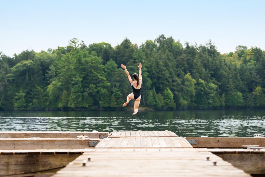 Woman jumping off dock into a lake with trees in the background